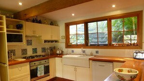 Uma cozinha com armários brancos, bancada de madeira, janela com vista para o verde, micro-ondas, fogão e lava-louças.