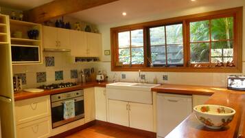 A kitchen with white cabinets, a wooden countertop, a window with a view of greenery, a microwave, a stove, and a dishwasher.