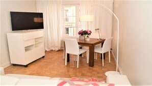 A modern living room with a flat-screen TV, a wooden dining table with white chairs, a white sofa, and a floor lamp. - Saint German des-Prés chic and comfortable (Paris)