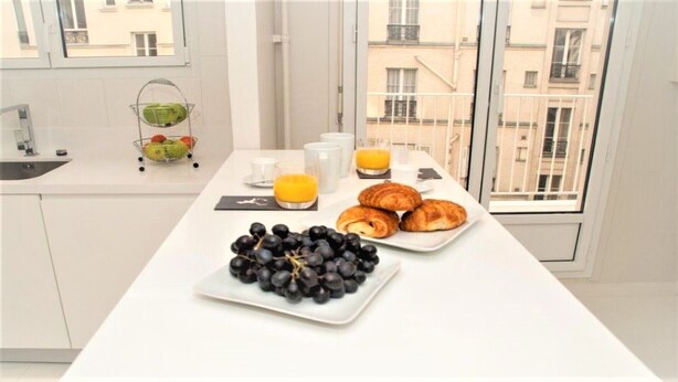 A breakfast setup with grapes, croissants, and orange juice on a white table in a modern kitchen with a city view. - Saint German des-Prés chic and comfortable (Paris)
