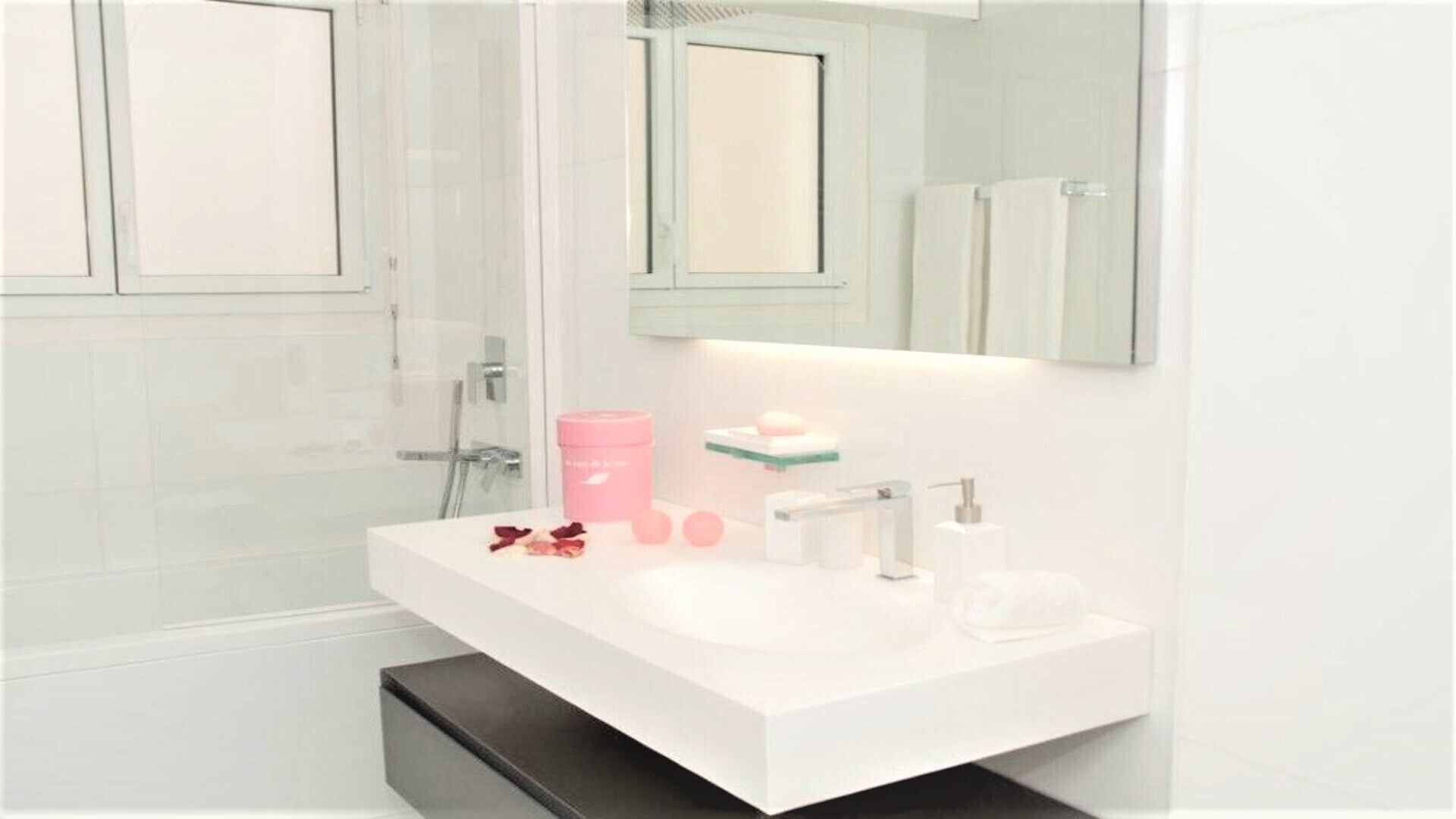 Un baño moderno con un lavabo blanco, un espejo y una zona de ducha.