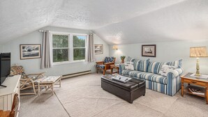 A cozy living room with a striped sofa, a small table, a television, and a window with curtains.