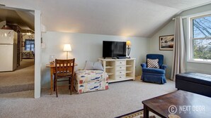 A cozy living room with a television, a blue armchair, a wooden table, and a patterned sofa.