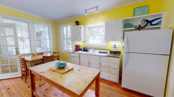 Una cocina con suelo de madera, armarios blancos, una mesa de madera y un refrigerador.