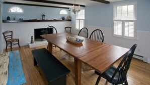 A dining room with a wooden table, chairs, a bench, a fireplace, and a chandelier. - 114 Long Pond Rd (Barnstable)
