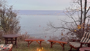 Un espace extérieur aménagé au bord du lac, avec un foyer, des tables et des chaises en bois.