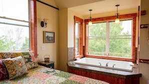 Une chambre avec un grand lit, une fenêtre donnant sur la forêt, une baignoire en bois et un tableau accroché au mur.