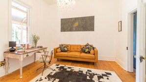 Ett vardagsrum med en soffa, ett skrivbord med en lampa, en kristallkrona och en stor, abstrakt målning på väggen.