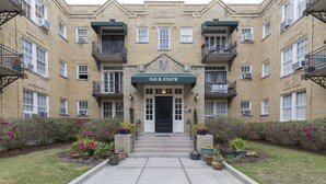 A multi-story building with a central entrance, balconies, and potted plants.
