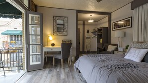 A bedroom with a bed, desk, chair, and a view of the outside balcony.