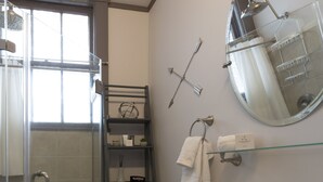 A bathroom with a glass shower enclosure, a white sink, and a glass shelf with towels and toiletries.