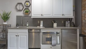 A modern kitchen with white cabinets, stainless steel appliances, a hexagonal backsplash, and a potted plant.