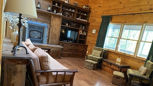 A cozy cabin interior with a wooden floor, a sofa, a chair, a television, and a fireplace. - Peaceful lakeside getaway (Meredith)