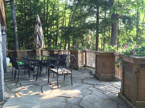 An outdoor patio with stone flooring, metal chairs, a glass table, and a wooden deck railing. - Peaceful lakeside getaway (Meredith)