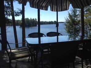 A covered outdoor seating area with a table and chairs, overlooking a lake with trees in the background. - Peaceful lakeside getaway (Meredith)