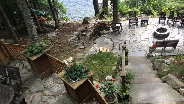 A stone patio with wooden furniture, a fire pit, and potted plants. - Peaceful lakeside getaway (Meredith)