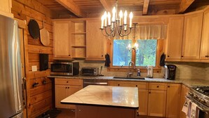 A kitchen with wooden cabinets, a central island, a stainless steel refrigerator, a microwave, a toaster, a sink, and a chandelier. - Peaceful lakeside getaway (Meredith)