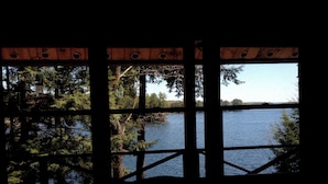 A view through a wooden structure with a metal railing, overlooking a calm body of water surrounded by trees. - Peaceful lakeside getaway (Meredith)