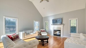 Un salón amplio con chimenea, sofás blancos y un televisor en la pared.