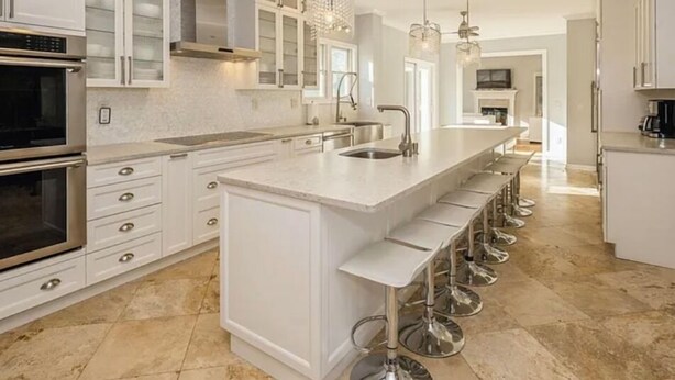 Una cocina moderna con armarios blancos, una isla grande con taburetes de bar, electrodomésticos de acero inoxidable e iluminación colgante.