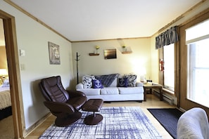 A living room with a leather recliner, a sofa with patterned cushions, a coffee table, and a view of the outdoors.
