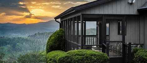 Ein modernes Haus mit überdachter Veranda, Blick auf die Berge und einem gepflegten Rasen.
