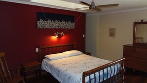 A bedroom with a bed, a wooden dresser, a chair, a ceiling fan, and a wall-mounted light fixture.