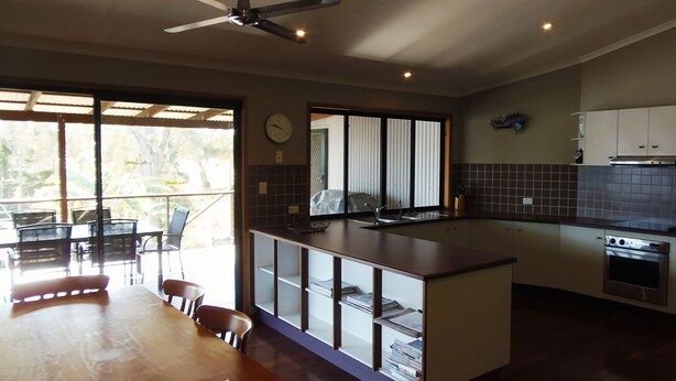 A modern kitchen with a central island, a dining area with a table and chairs, and a view through large windows.