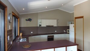A compact kitchen with a dark countertop, white cabinets, and a tiled backsplash.