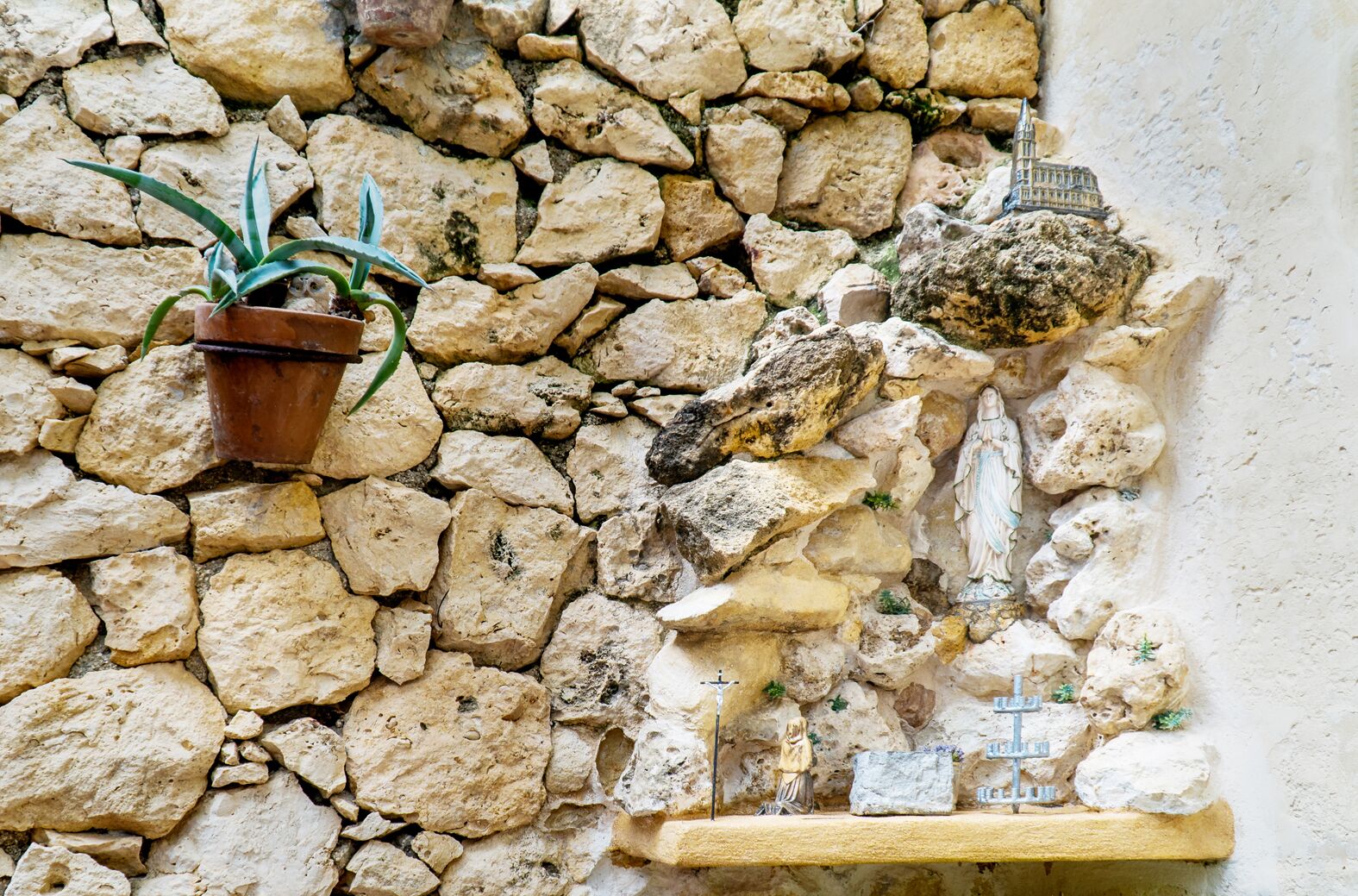 Un muro de piedra con una planta en maceta y una estatua.