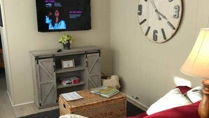 Ein Wohnzimmer mit einem roten Sofa, einer großen Wanduhr, einem an der Wand befestigten Fernseher und einem kleinen Tisch mit einer Lampe.