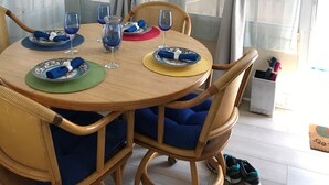 Ein runder Holztisch mit blau gepolsterten Stühlen, umgeben von hellen Vorhängen und einer hängenden Lampe.