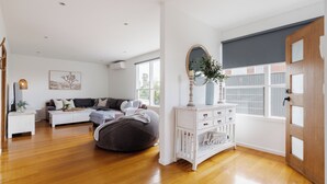 Ein geräumiges Wohnzimmer mit großem Fenster, einem grauen Sitzsack, einem weißen Sofa und einer weißen Kommode mit Spiegel.