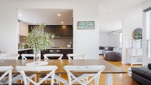 Ein modernes Wohnzimmer mit einem Holzesstisch, weißen Stühlen, einem grauen Sofa und einer Küche im Hintergrund.