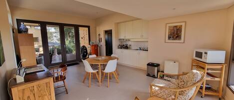 A modern kitchen with white cabinets, a dining area with a round table and chairs, a sofa, and a microwave on a cart.