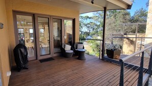Una terraza de madera con mobiliario exterior, una puerta corrediza de vidrio que da a un espacio interior y una pared de piedra.