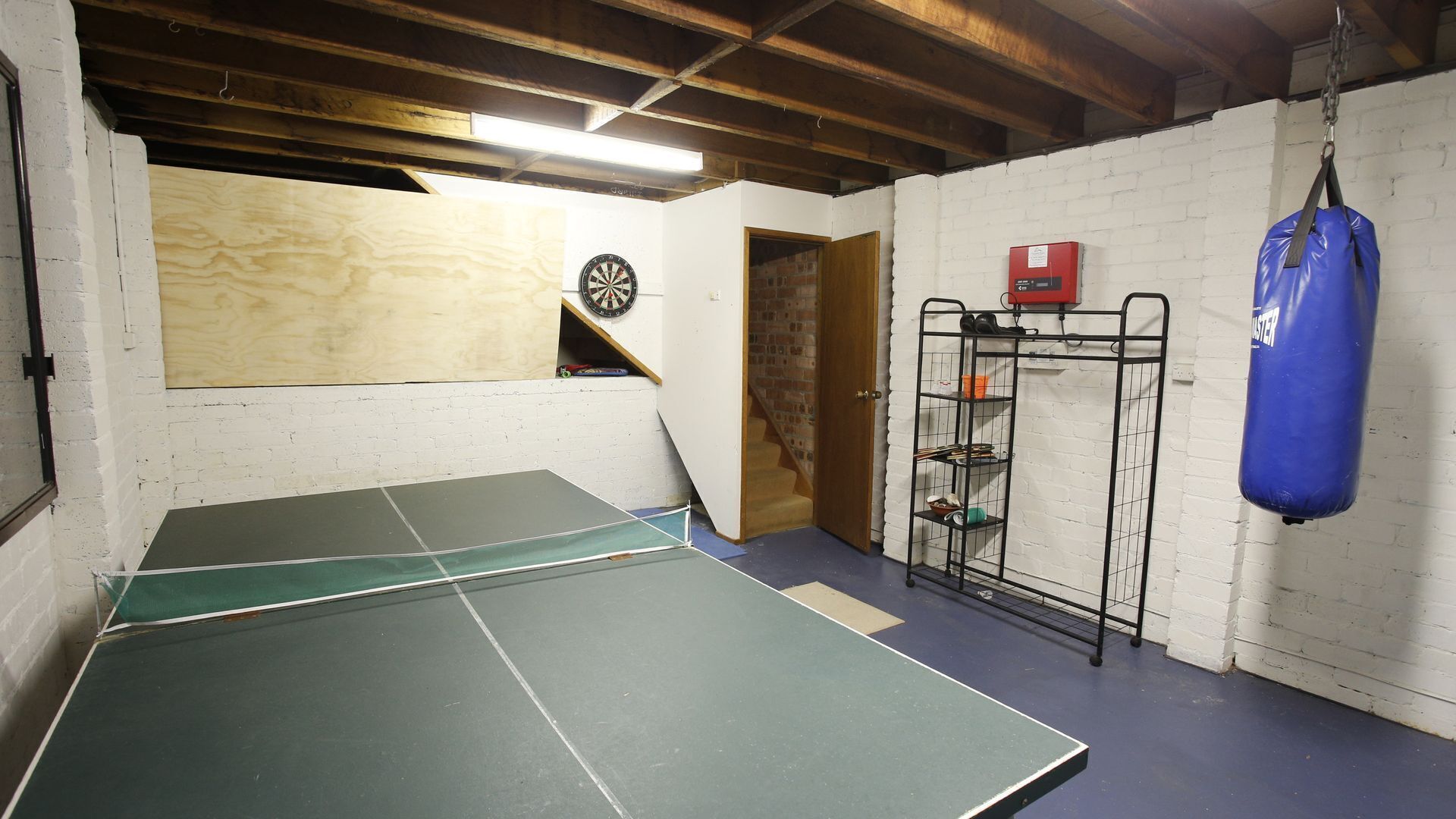 A ping pong table in a room with a dartboard, a punching bag, and a shelf with shoes.