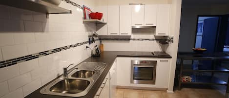 A modern kitchen with white cabinets, a stainless steel sink, and a built-in oven.