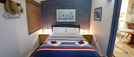A neatly made bed with striped bedding, a painting of fish on the wall, and a small table with a chair in the corner.