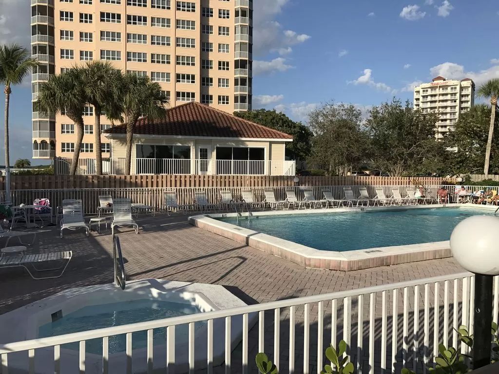 A hotel pool area with lounge chairs, a hot tub, and a view of high-rise buildings.