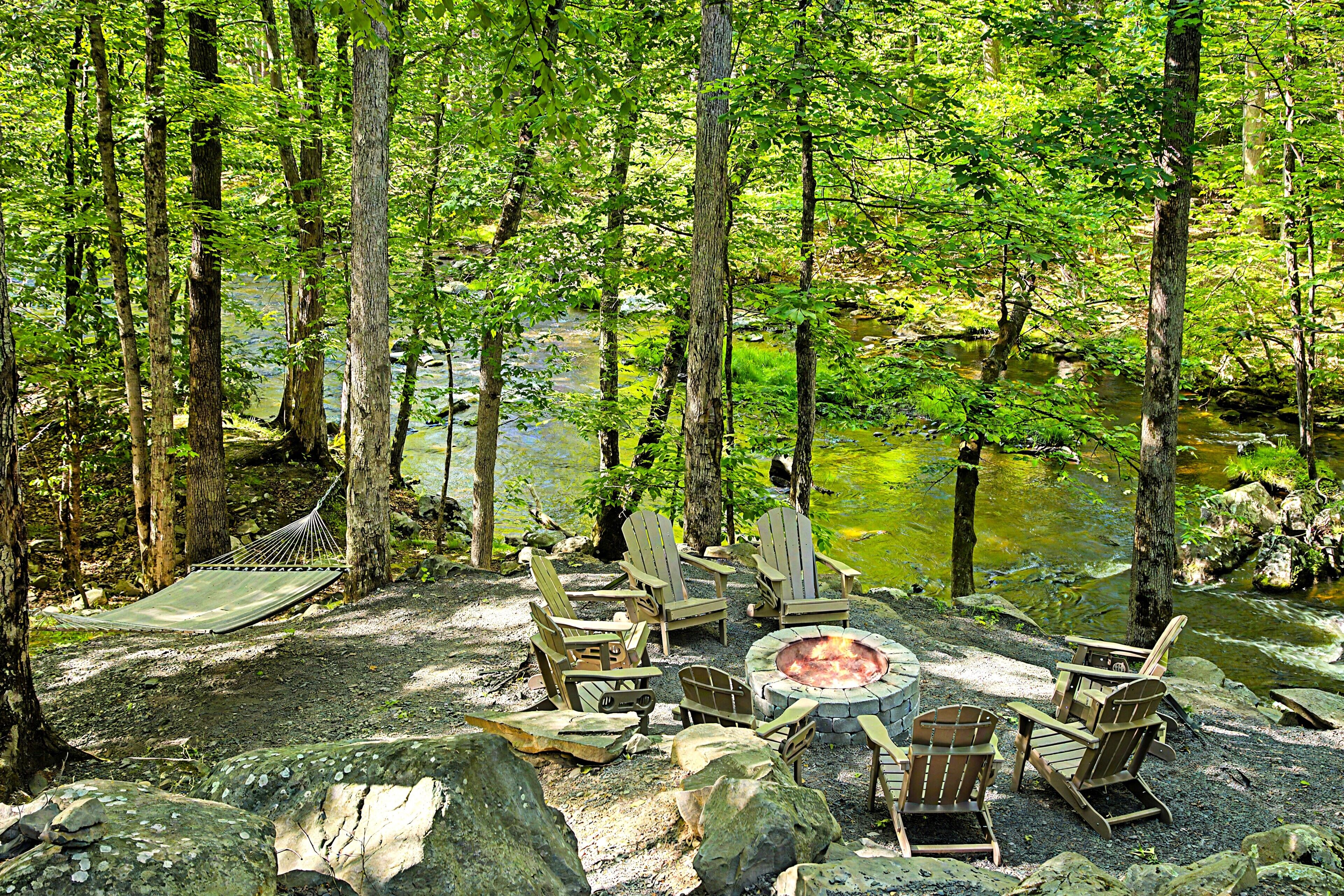 Un terrain de camping situé dans une forêt, équipé d’un foyer et de chaises Adirondack.
