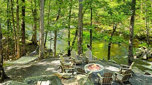 En campingplats i skogen med en eldstad och Adirondack-stolar.
