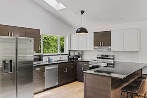 A modern kitchen with stainless steel appliances, dark wood cabinets, and a large window providing natural light.