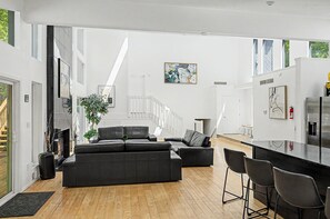 Ein modernes Wohnzimmer mit Kamin, schwarzen Ledersofas, einem Essbereich mit Barhocker und einer Treppe, die zu einer oberen Ebene führt.