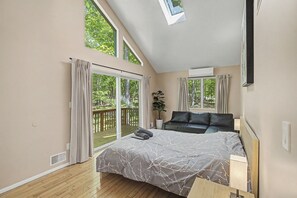 A bedroom with a large bed, a sofa, a potted plant, and a view of a balcony. - Modern Stream-front property with hot tub. (Bushkill)