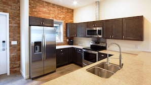 A modern kitchen with dark cabinets, stainless steel appliances, and a brick accent wall.