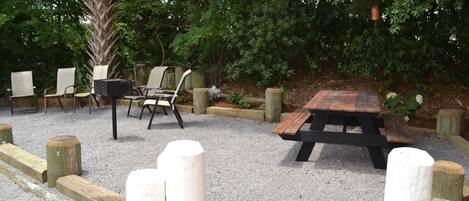 An outdoor seating area with a wooden table and chairs, surrounded by a gravel path and wooden bollards.