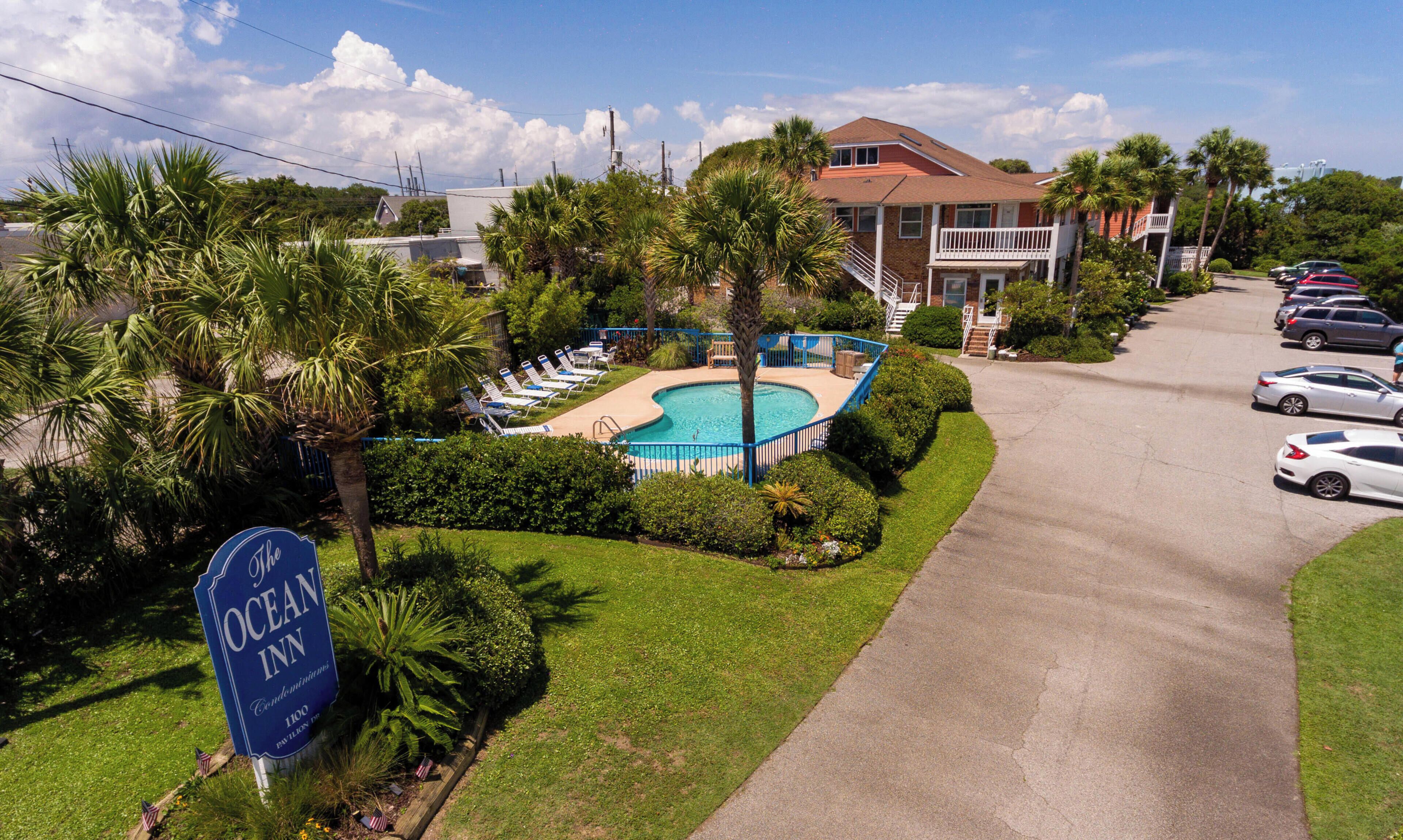 A hotel with a swimming pool, a sign reading "The Ocean Inn," and a parking area with cars.