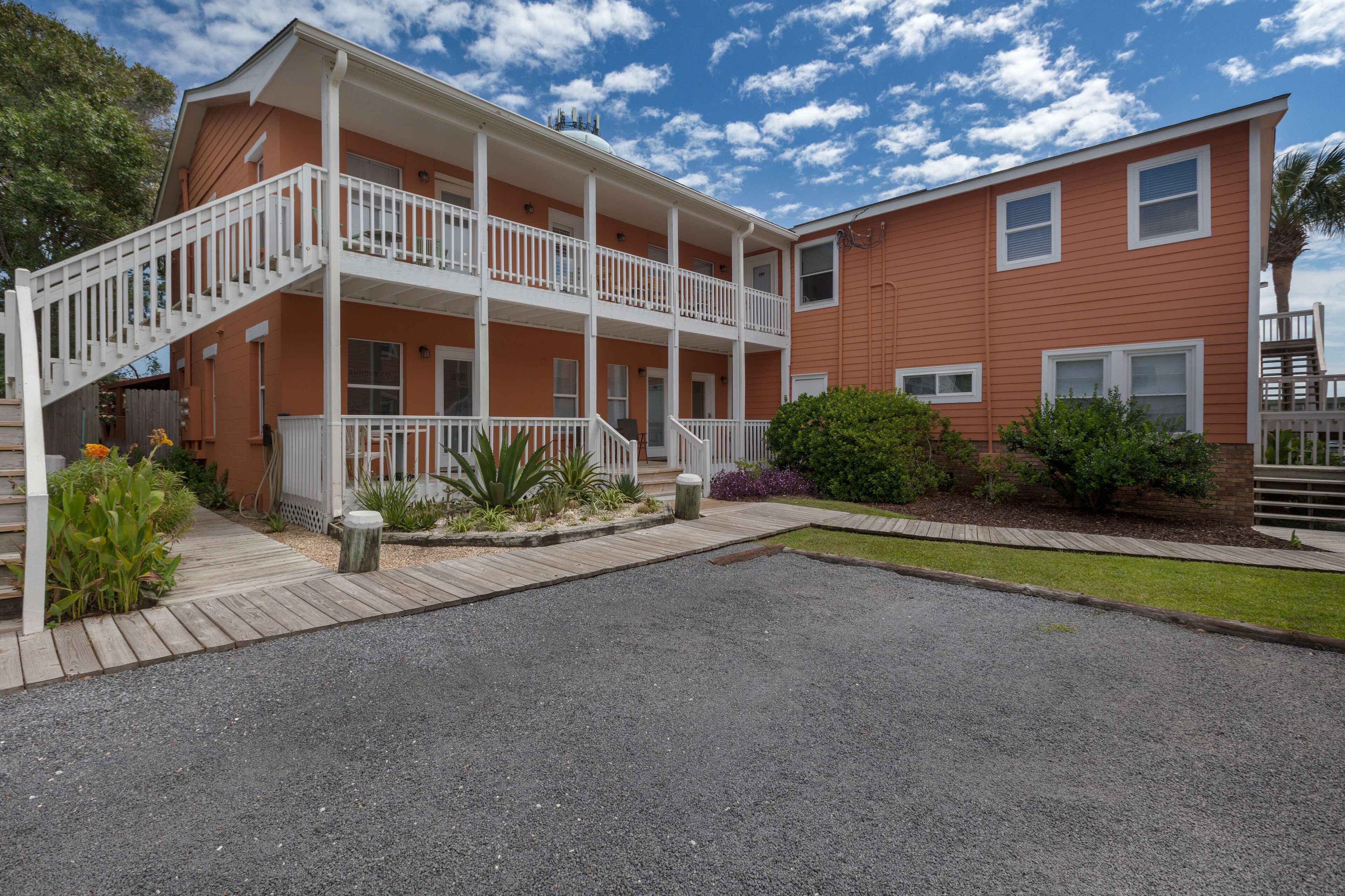 A two-story building with a balcony, a covered porch, and a gravel driveway.