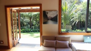 Una habitación con sofá, un cuadro y vista a un jardín por una ventana.